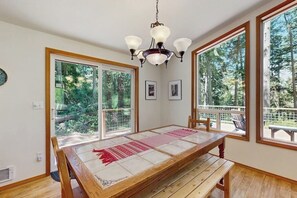 Ein Essbereich mit Holztisch, Stühlen, einem Kronleuchter, großen Fenstern und gerahmten Bildern an der Wand.