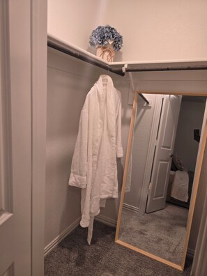 Une salle de bain avec un peignoir blanc suspendu à un porte-serviettes, un miroir et une décoration florale bleue sur le mur.