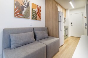 Ein modernes Wohnzimmer mit einer grauen Couch, einem weißen Kühlschrank und einer Küche im Hintergrund.