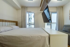 Ein Hotelzimmer mit einem Bett, einem an der Wand befestigten Fernseher, einem Sofa und einem Fenster mit Vorhängen.