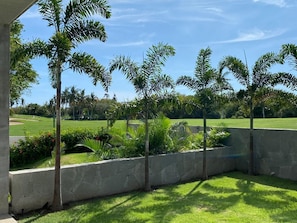 Eine angelegte Grünfläche mit Palmen, einer Steinmauer und Blick auf einen Golfplatz.