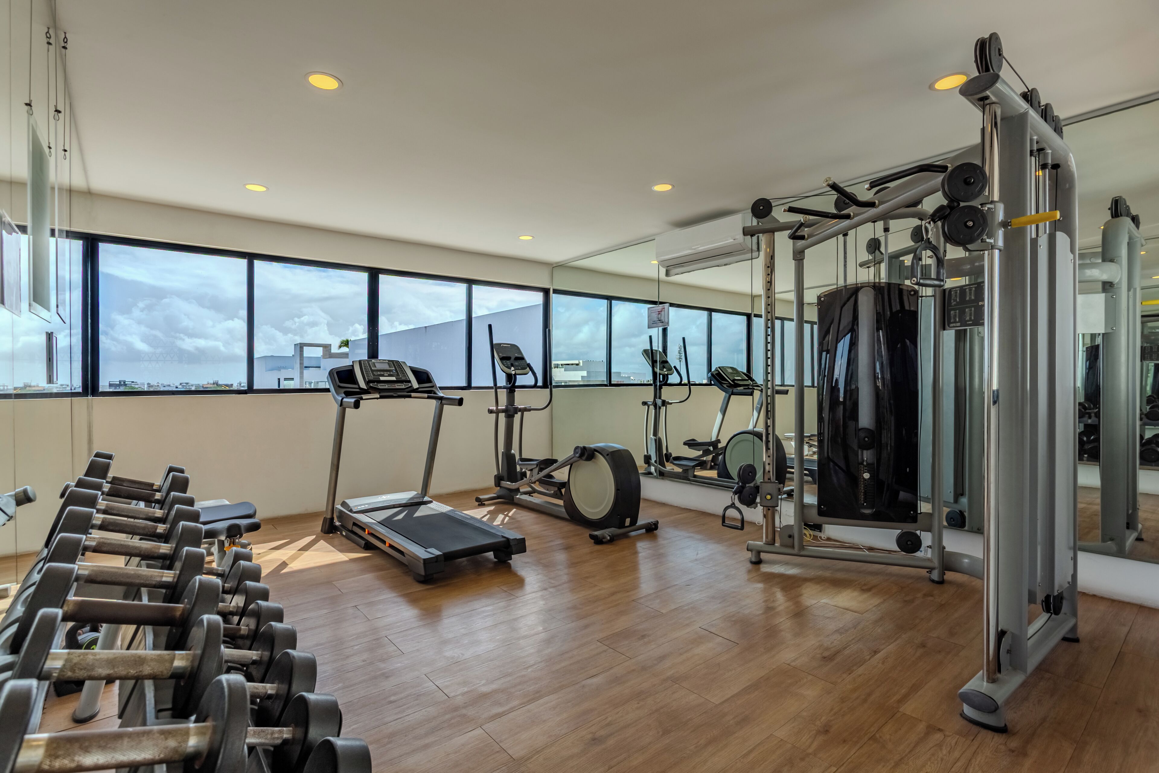 Ett gym med träningsutrustning, stora fönster och ett trägolv.