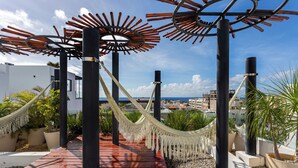 Una terraza de madera con una hamaca, plantas en macetas y vistas de la ciudad.