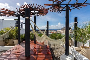 A wooden deck with a hammock, potted plants, and a view of the city.