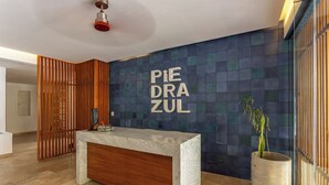 Un mostrador de recepción con encimera de mármol y base de madera, una planta en maceta y una pared con un diseño geométrico y el texto 'PIE DRA ZUL'.