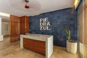 A reception desk with a marble top and wooden base, a potted plant, and a wall with a geometric pattern and the text 'PIE DRA ZUL'.
