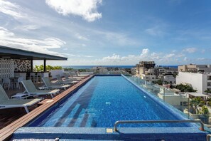 A rooftop infinity pool with lounge chairs, a bar area, and a view of the cityscape and ocean. - Studio in a prime location, just a few meters from 5th Street and the beach (Playa del Carmen)