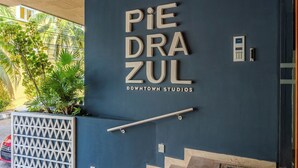 Entrada de un edificio con un letrero que dice 'PIEDRA ZUL DOWNTOWN STUDIOS' y una escalera que sube.