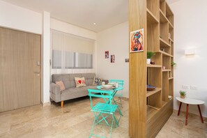 A living room with a sofa, a coffee table, a teal chair, a wooden bookshelf, and a small white table. - Studio in a prime location, just a few meters from 5th Street and the beach (Playa del Carmen)