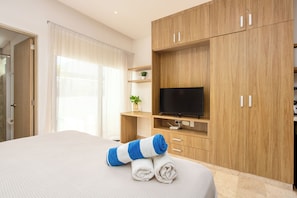 A hotel room with a bed, a TV, wooden cabinets, and a window with curtains. - Studio in a prime location, just a few meters from 5th Street and the beach (Playa del Carmen)