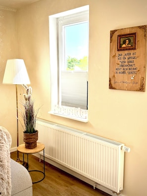 A room with a window, a radiator, a lamp, and a framed quote on the wall.