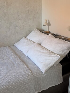 A bed with white bedding, a lamp on a bedside table, and a textured wall.