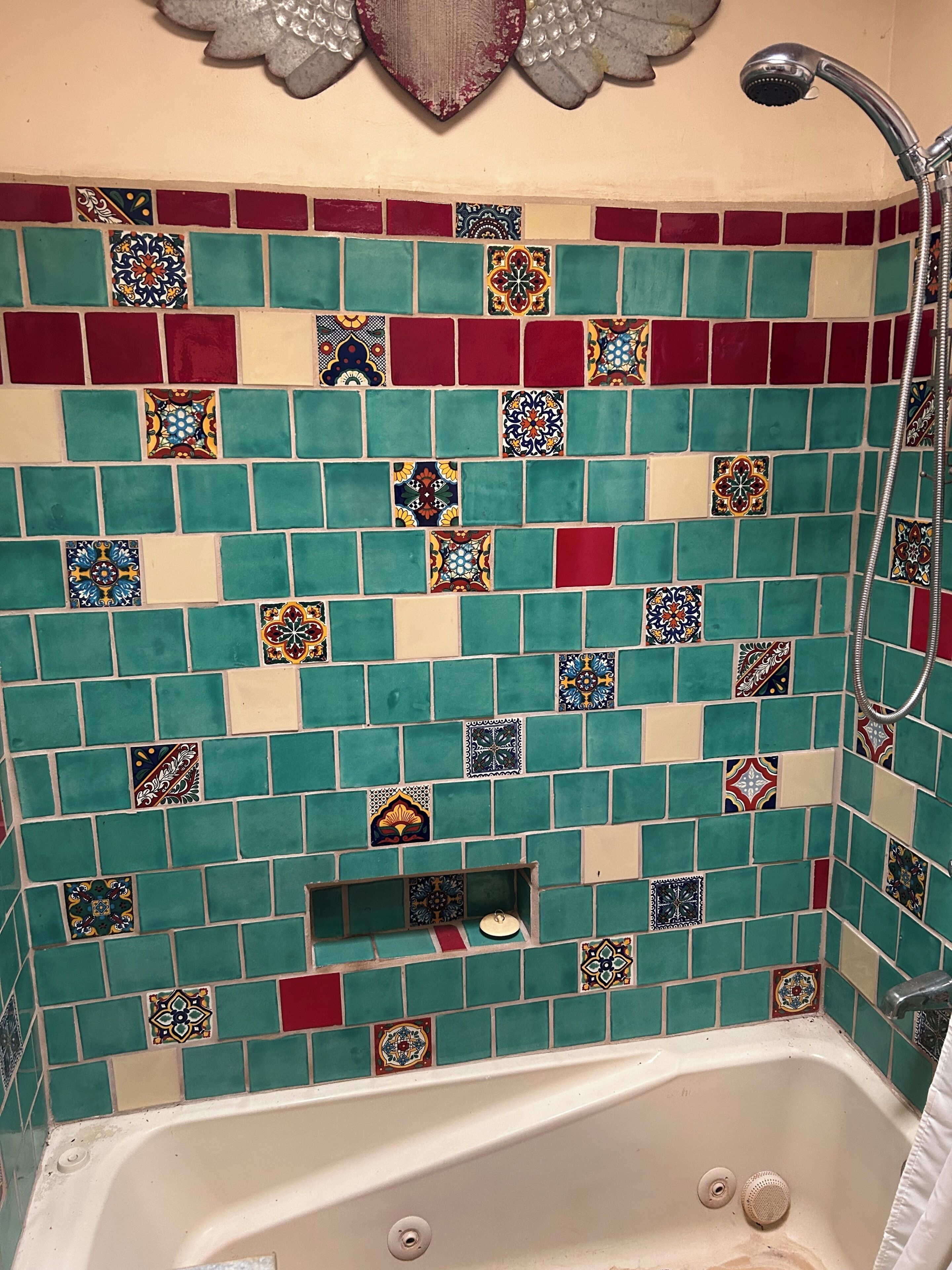 Un baño con bañera, ducha y pared revestida de azulejos cuadrados y rectangulares en varios colores.