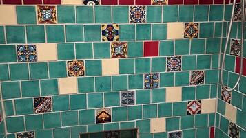 Un baño con bañera, ducha y pared revestida de azulejos cuadrados y rectangulares en varios colores.
