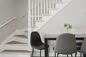 A staircase with white railings and wooden steps, a dining table with chairs, and a vase with flowers. - Modren 4BD 2BA Home Near Downtown / Metra (Highland Park)