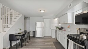 Uma cozinha moderna com armários brancos, um fogão de aço inoxidável e uma área de refeições com mesa e cadeiras.