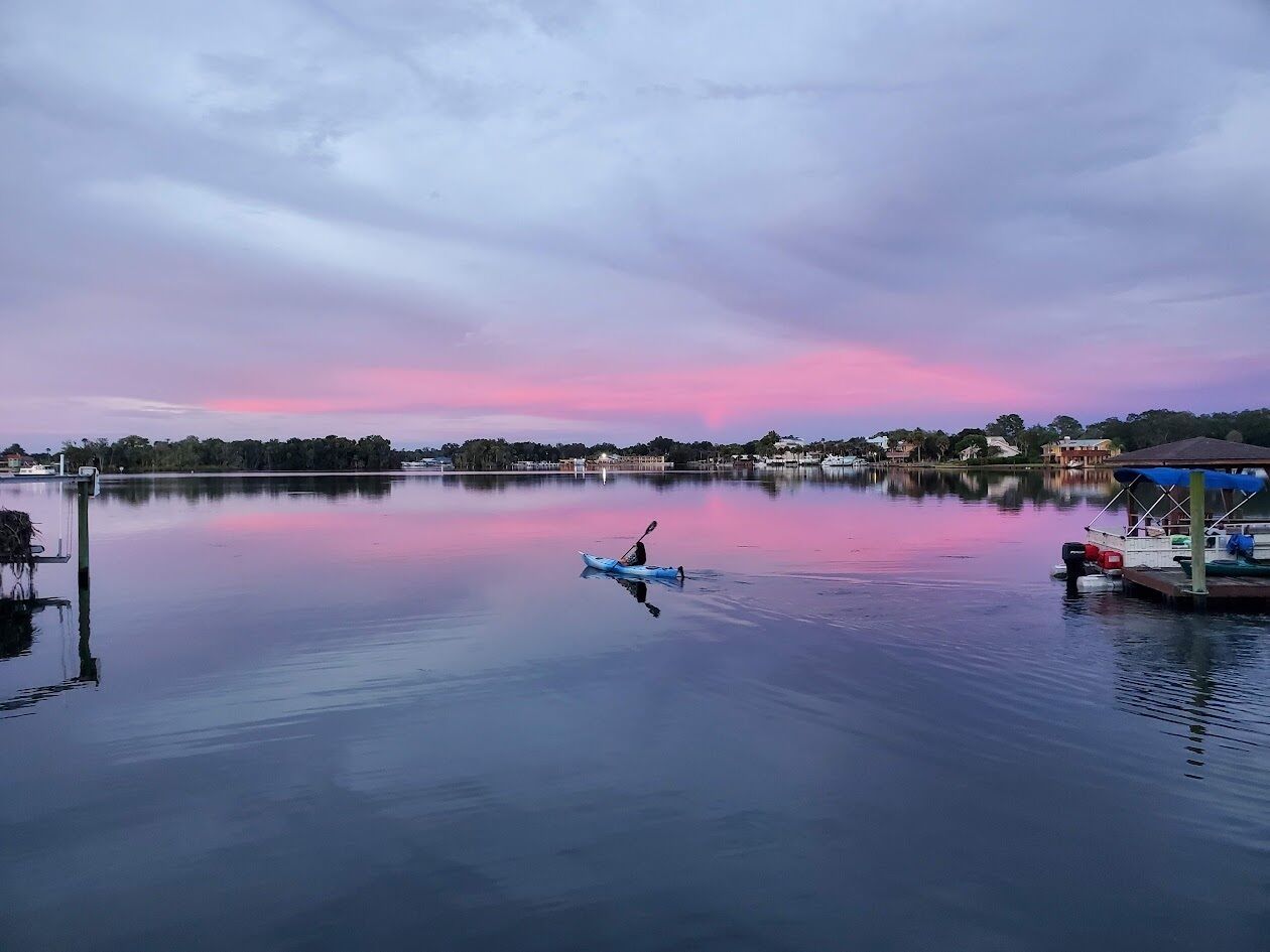 A calm lake at dusk with a kayak in the center, a dock on the left, and a covered boat on the right.
