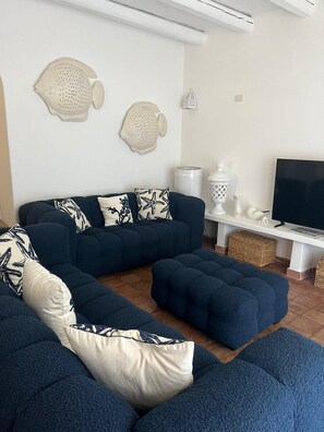 A modern living room with a dark blue sectional sofa, a flat-screen TV, decorative fish wall art, and a white console table. - Relax in Villasimius (Villasimius)