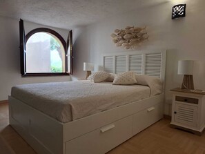 A bedroom with a bed, bedside tables, a window, and a wall decoration. - Relax in Villasimius (Villasimius)