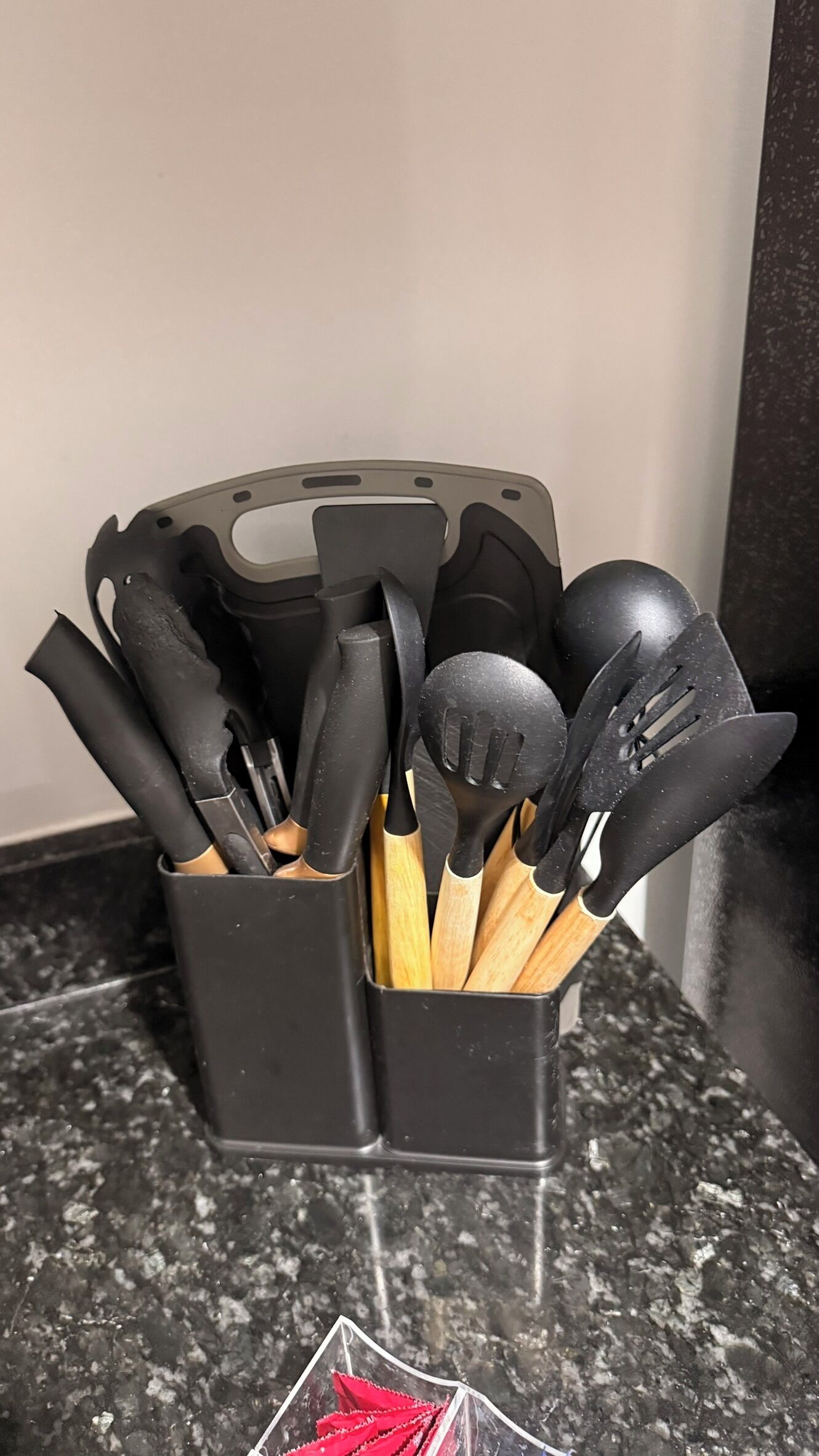 A black utensil holder with various kitchen tools on a granite countertop.