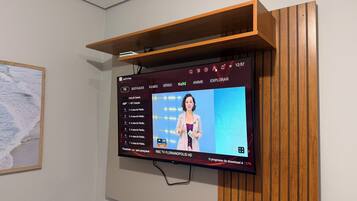 A flat-screen TV mounted on a wall with a wooden shelf above it.