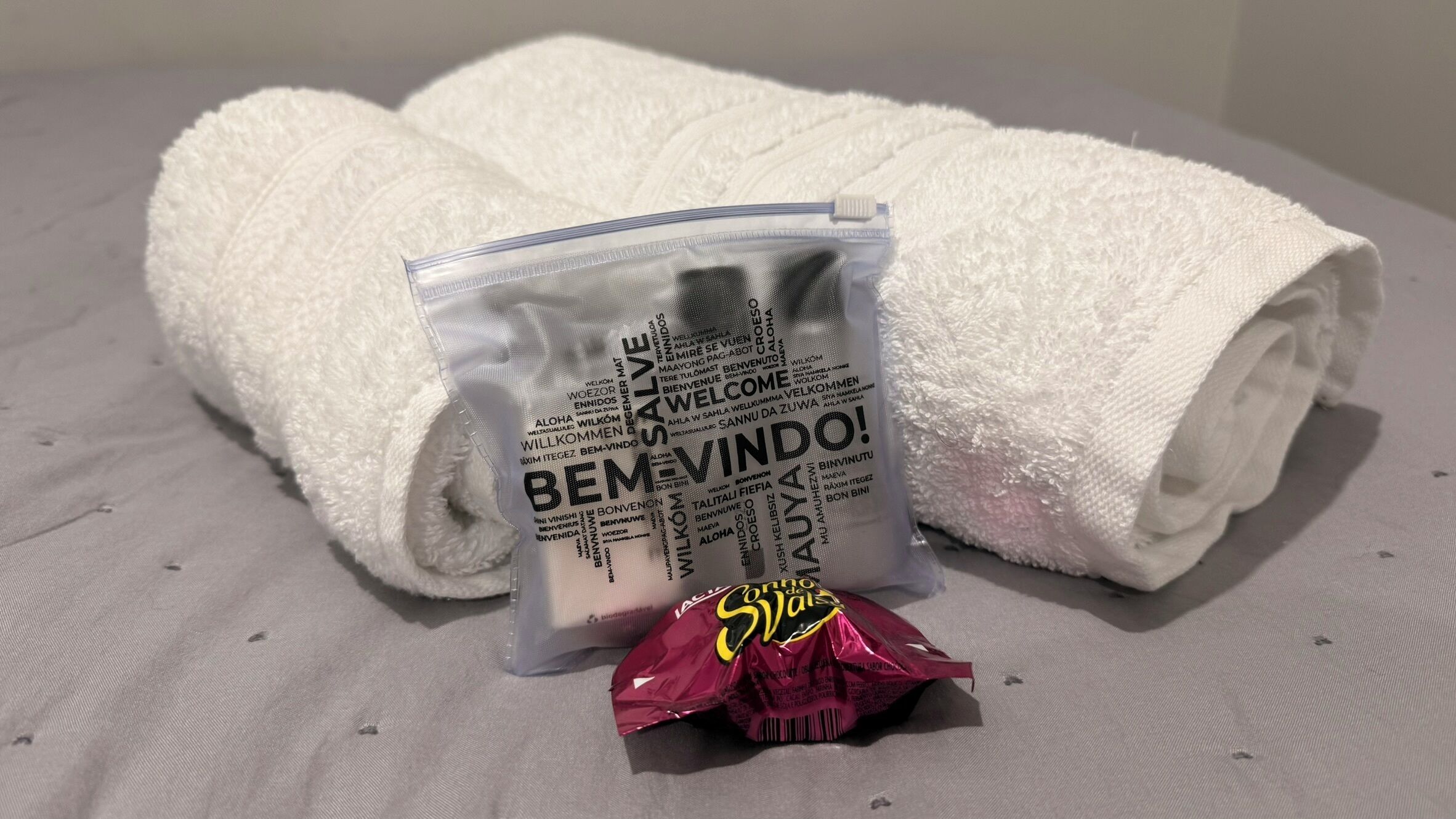 A white towel, a small transparent bag with text, and a red packet on a grey surface.