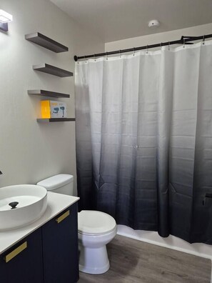 A bathroom with a white sink, two toilets, a black shower curtain, and a light fixture on the wall. - Entire Home in Dover, DE/Close to Raceway/Casino (Dover)