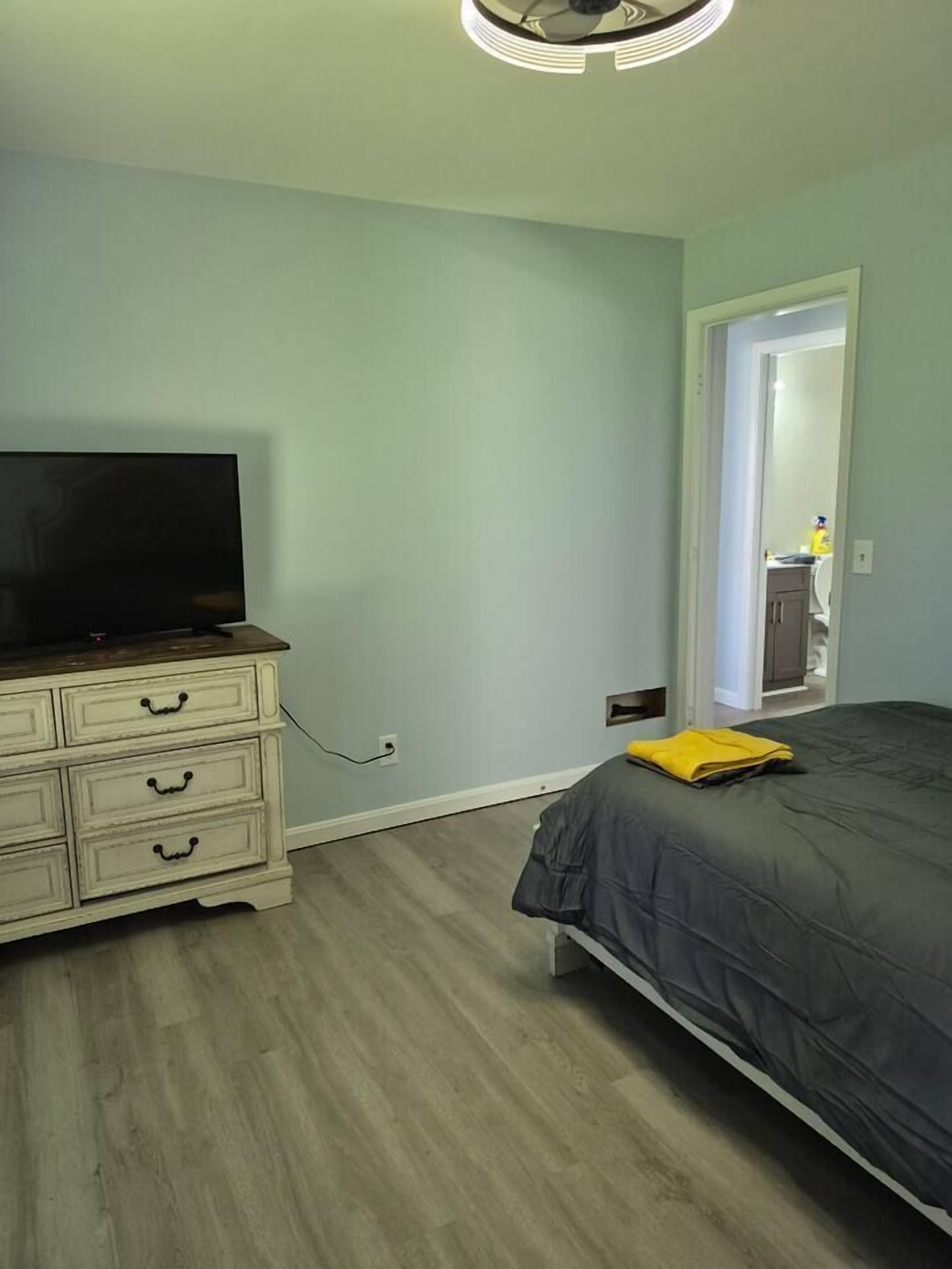 Une chambre à coucher comprenant un lit, une commode, un téléviseur et une porte donnant sur une salle de bain.