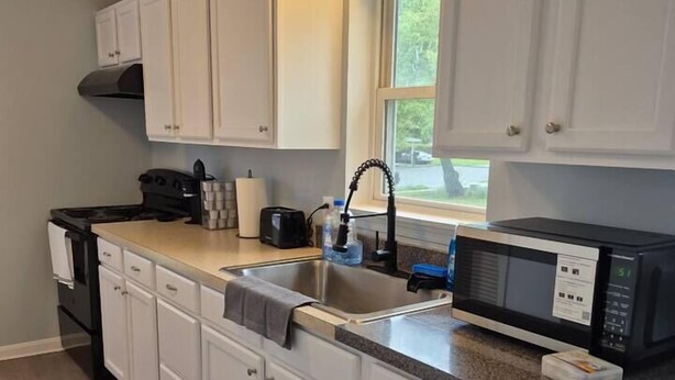A kitchen with white cabinets, a granite countertop, a stove, a microwave, and a window. - Entire Home in Dover, DE/Close to Raceway/Casino (Dover)