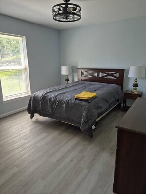 A bedroom with a bed, two bedside lamps, a wooden headboard, a window with blinds, and a wooden dresser. - Entire Home in Dover, DE/Close to Raceway/Casino (Dover)
