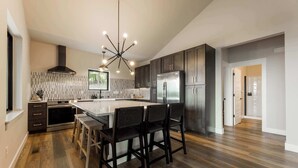 Una cocina moderna con una isla central, muebles oscuros, electrodomésticos de acero inoxidable y una lámpara de techo original.