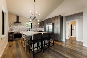 A modern kitchen with a central island, dark cabinetry, stainless steel appliances, and a unique chandelier. - Oak Ridge on Beaver Lake, 5BR Lakeview, Sleeps 13 (Garfield)