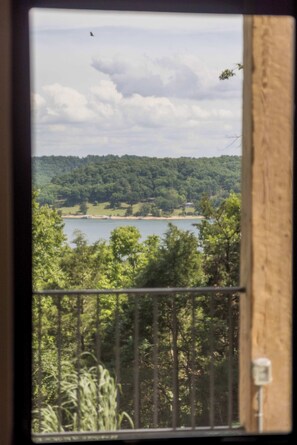 A view through a window of a natural landscape with a lake, forest, and a distant house. - Oak Ridge on Beaver Lake, 5BR Lakeview, Sleeps 13 (Garfield)