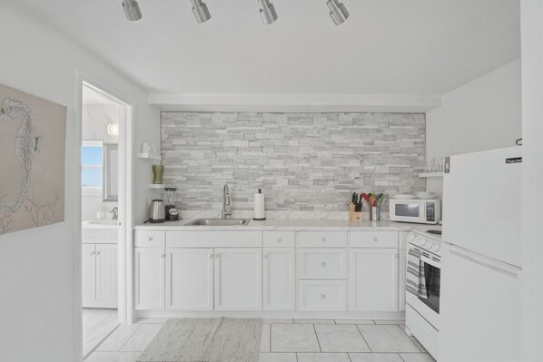 A modern kitchen with white cabinets, a stone backsplash, and a built-in oven.