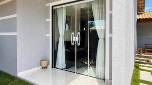 A modern house with a glass door, a small outdoor seating area, and a well-maintained lawn. - Refúgio Unamar - Cabo Frio RJ (Cabo Frio)