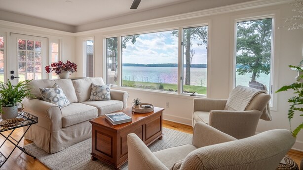 Una sala de estar con sofá, sillones, una mesa de centro y ventanas amplias con vista a un lago.