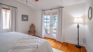 Un dormitorio con cama, una silla, lámpara de pie, ventilador de techo y vista a través de un ventanal.