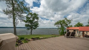 Terraza de madera con mobiliario exterior, una parrilla y vistas a un lago.