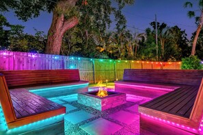A wooden outdoor seating area with a fire pit, surrounded by colorful LED lights. - The Rainbow Lagoon - Pickleball, Heated Pool, Golf (Bradenton)