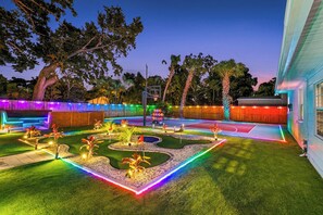 A well-lit outdoor area with a basketball court, a small garden, and a wooden fence. - The Rainbow Lagoon - Pickleball, Heated Pool, Golf (Bradenton)
