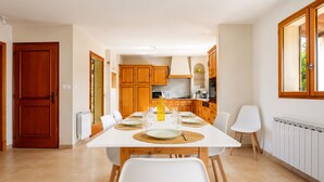A dining area with a white table set for four, wooden cabinets, and a kitchen in the background.
