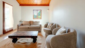 A living room with a wooden ceiling, a sofa, a chair, a coffee table, and a window with a view.