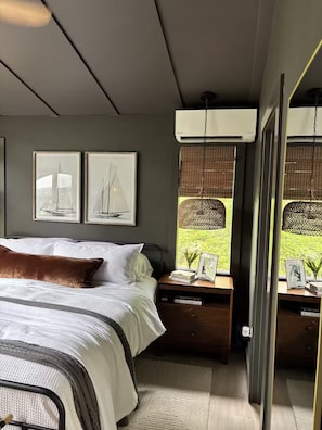 Ein Schlafzimmer mit Bett, Nachttischen, gerahmten Bildern und Blick auf Grünflächen.