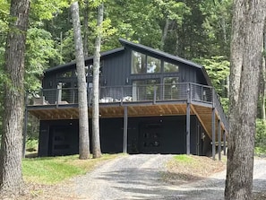 Eine moderne, zweistöckige Holzhütte mit einer Holzterrasse und einer überdachten Garage.