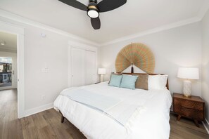 A bedroom with a bed, bedside lamps, a ceiling fan, a wall-mounted decorative item, and a door. - Palm Springs at The Cove Riverwalk Villas (Wilmington)