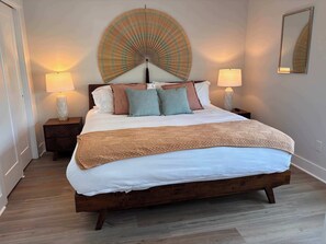 Ein Schlafzimmer mit einem großen Bett, zwei Nachttischen mit Lampen, einem Wandspiegel und einem dekorativen Ventilator.