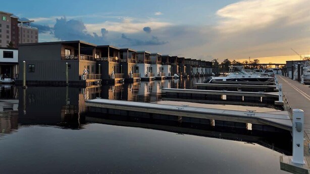 A marina with docked boats, a calm water surface, and a row of buildings with balconies. - Palm Springs at The Cove Riverwalk Villas (Wilmington)