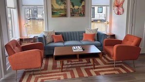 A living room with a grey sofa, orange armchairs, a wooden coffee table, and two paintings on the wall. - Palm Springs at The Cove Riverwalk Villas (Wilmington)