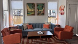A living room with a sofa, two armchairs, a coffee table, a ceiling fan, and artwork on the wall. - Palm Springs at The Cove Riverwalk Villas (Wilmington)