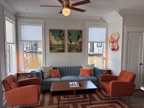 Ein Wohnzimmer mit einer Couch, zwei Sesseln, einem Couchtisch, einem Deckenventilator und Kunstwerken an der Wand.